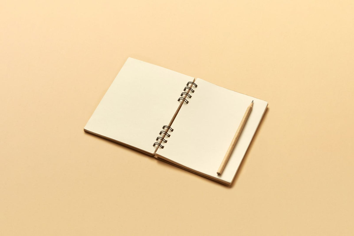 Open cream notebook with a wooden pencil on a beige background / دفتر كريميّ مفتوح مع قلم خشبي على خلفية بيج