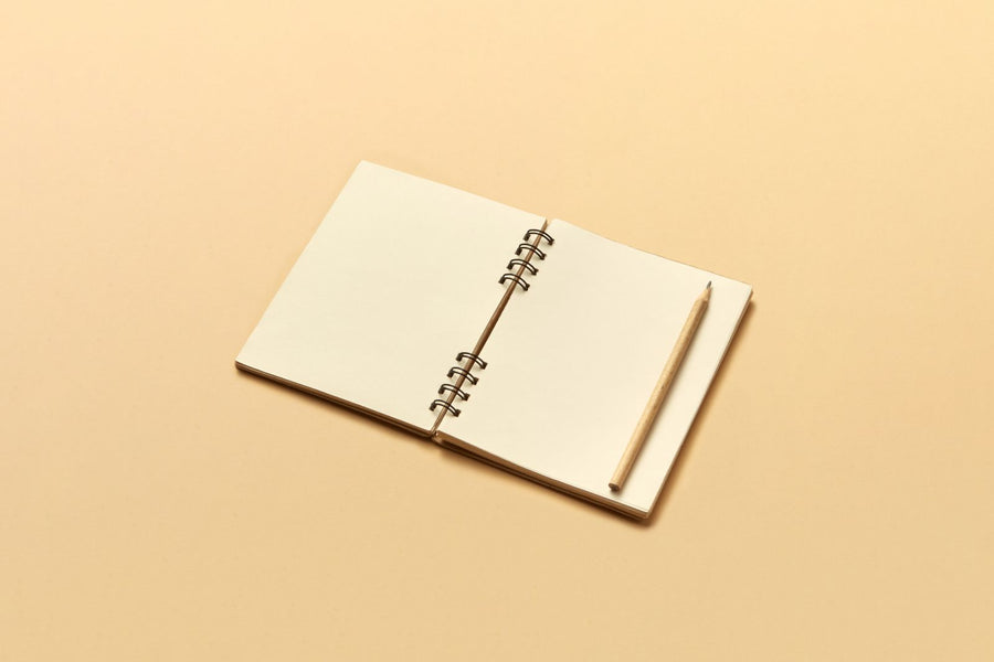 Open cream notebook with a wooden pencil on a beige background / دفتر كريميّ مفتوح مع قلم خشبي على خلفية بيج
