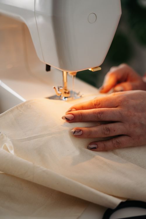 Hands guiding cream fabric through a sewing machine / يدان توجّهان قماشاً كريميّ اللون عبر ماكينة خياطة