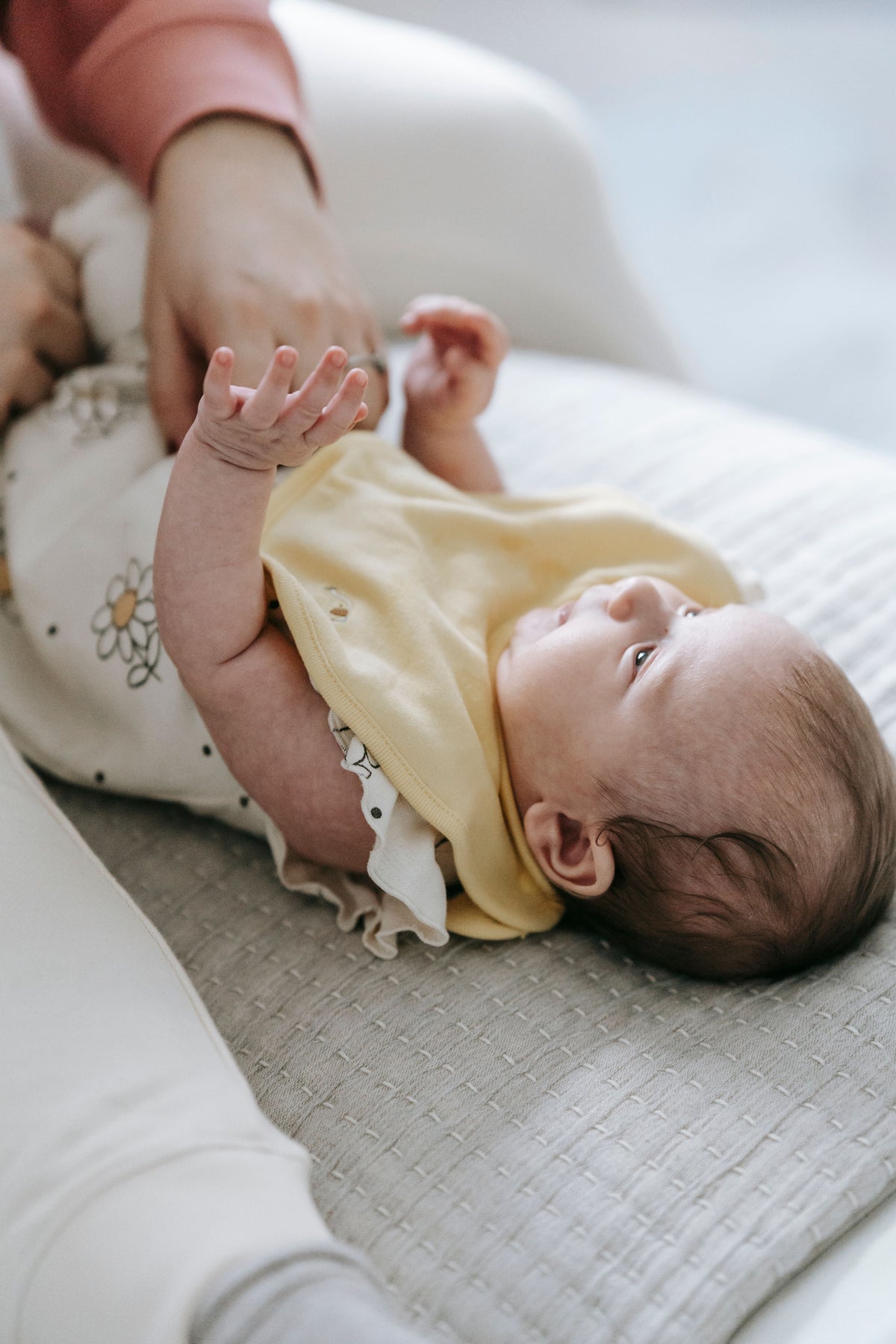Faceless parent dressing a newborn on a light couch | أحد الوالدين يلبّس مولوداً على أريكة فاتحة