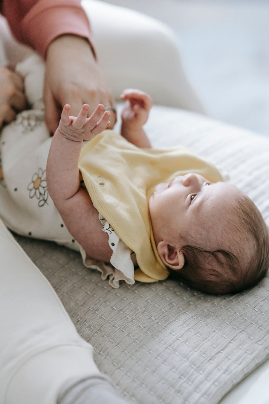 Faceless parent dressing a newborn on a light couch | أحد الوالدين يلبّس مولوداً على أريكة فاتحة