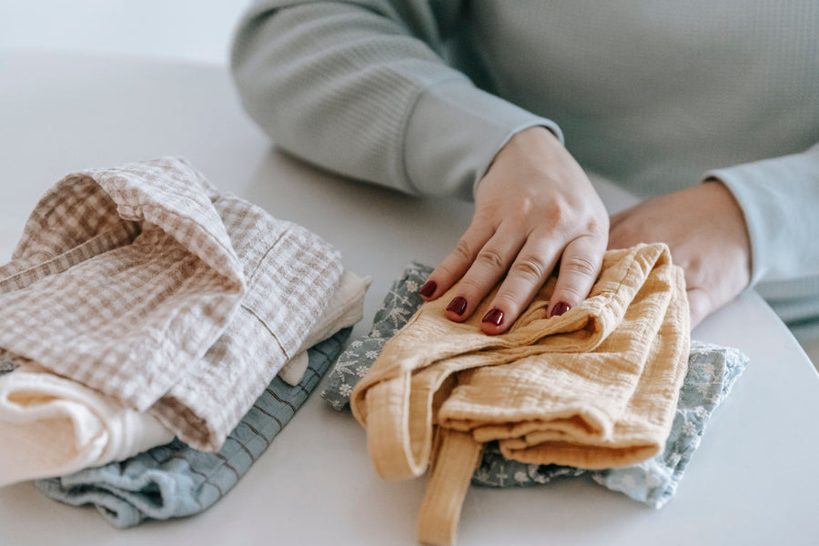 Caregiver folding neutral baby clothes into a neat stack | شخص يرتّب ملابس بيبي بألوان هادئة في رزمة صغيرة
